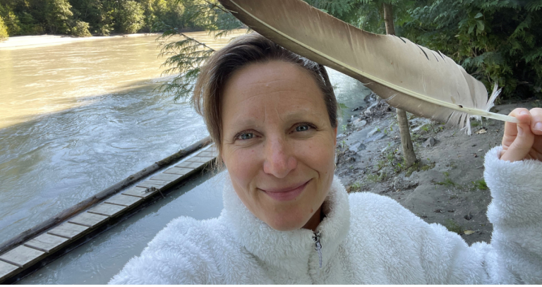 Veronica Woodruff poses with a feather near a river.